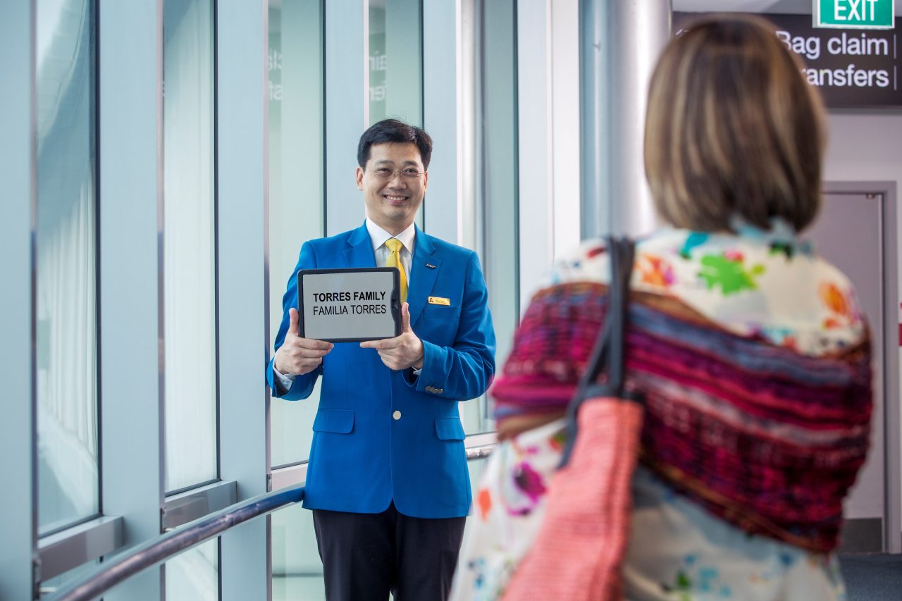 bluecoat wearing man waits for traveller at arrivals gate holding sign that says torres family